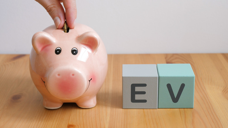Fingers depositing a coin into a piggy bank next to E and V letter blocks