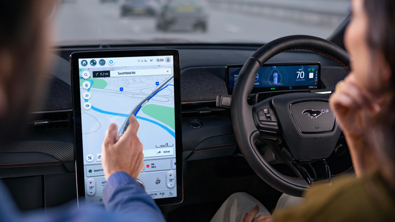 A person touching the car's navigation screen while someone else drives.
