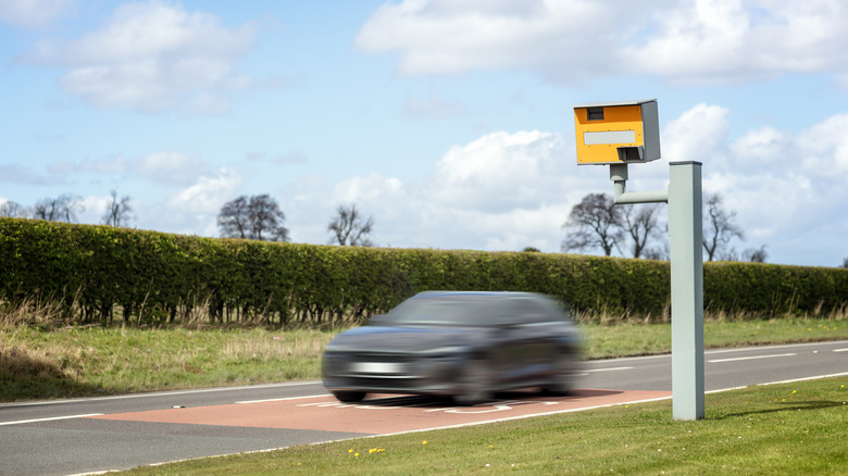 A blurred vehicle traveling quickly past a speed camera positioned roadside on European country motorway