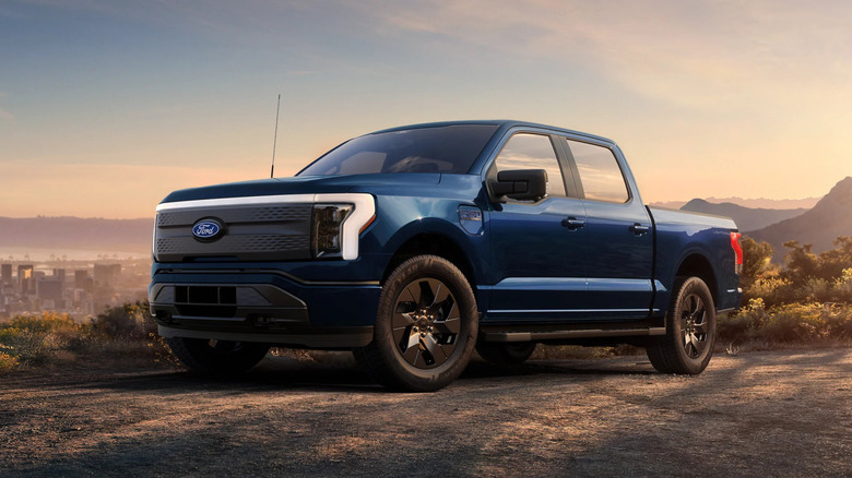 2025 Ford F-150 Lightning electric pickup truck parked on a scenic overlook with city skyline and mountains at sunset
