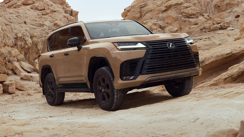 Tan Lexus LX 700h luxury SUV navigating rugged desert terrain with large rock formations in the background