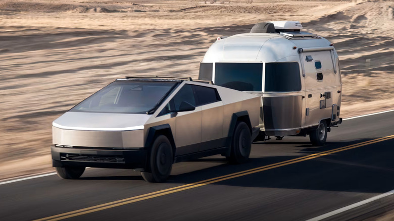 A cybertruck towing a caravan down an arid landscape on a road with mountains visible in the background