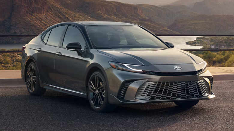 A toyota camry 2025 hybrid model parked against a reservoir of water with hills visible in the background, in the evening