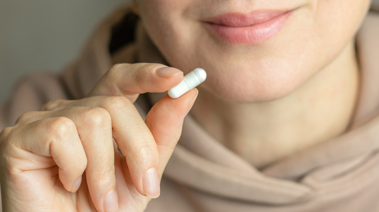 A woman holding a single capsule which is near the size of the bioresorbable battery from MIT researchers