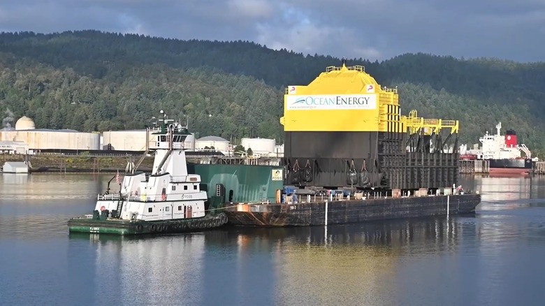An OceanEnergy wave-power buoy on a barge close to the shore, being manoeuvred by a tug boat.