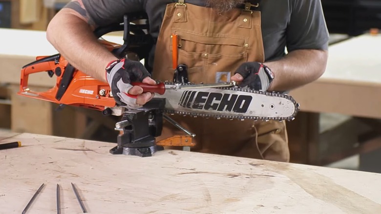 A man using a guide and file to sharpen a chainsaw chain