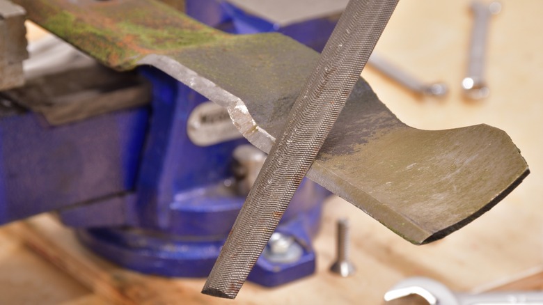 Sharpening a lawn mower blade with a file.