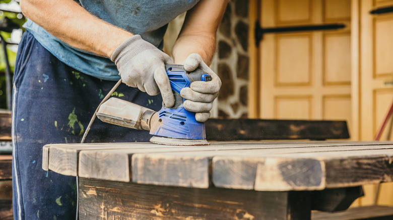 Man using blue sander on wooden table