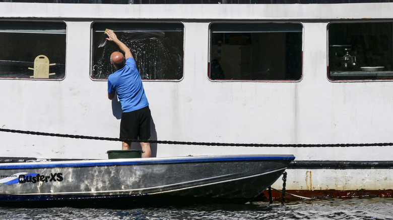 person washing the window of a houseboat from another smaller boat