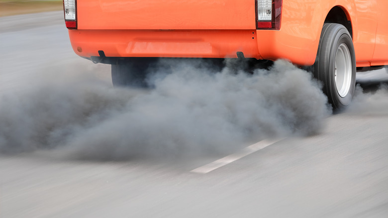 An orange diesel pickup truck with no rear bumper, emitting lots of smoke from its exhaust.
