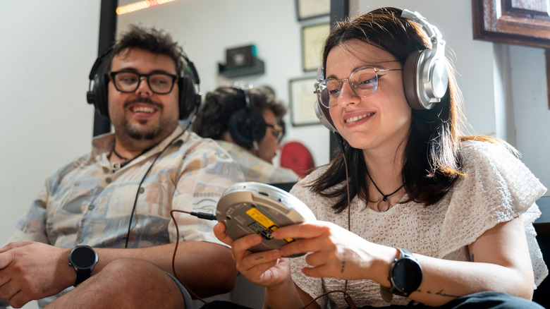 Two people listening to a Sony Walkman using large headphones.