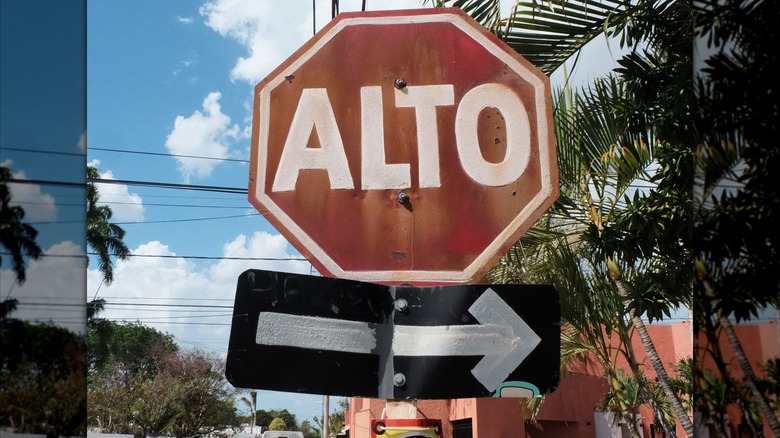 A worn "Alto" stop sign with an arrow pointing right. The sign is weathered, with faded paint and a blue sky in the background.