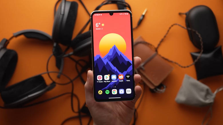 LG V60 held in hand over other electronics on table