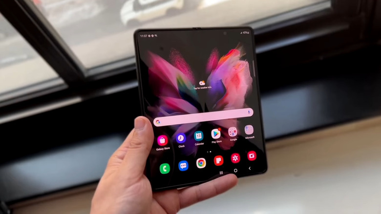 A person holding the Samsung Galaxy Z Fold 3 in front of a window overlooking the street