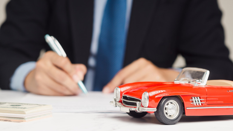 A person signing a contract with a model car in the foreground