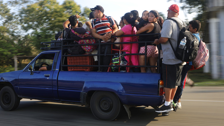 A crowd of people stand on the back of a blue pickup truck while moving