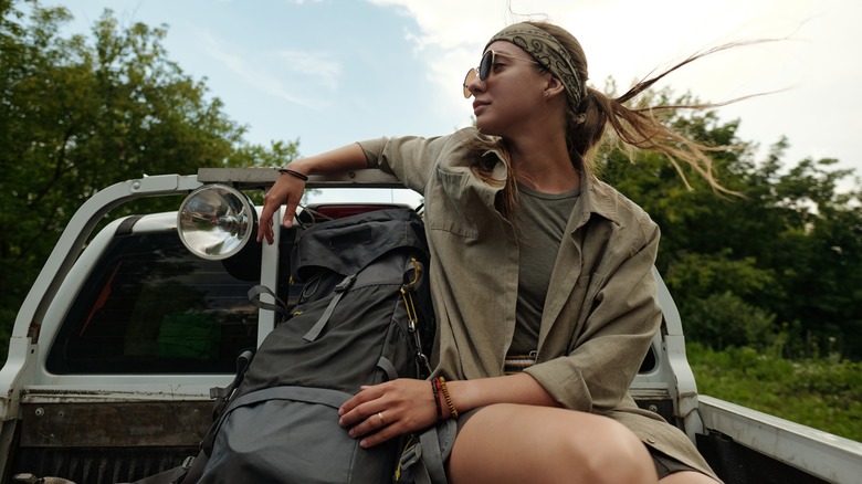 A woman sits on the back of a pickup truck with a backpack