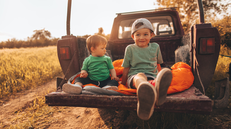 Two boys sit on the open tailgate of a pickup truck