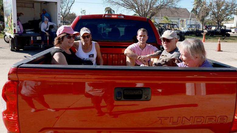 Five people sit in the bed of a red pickup truck