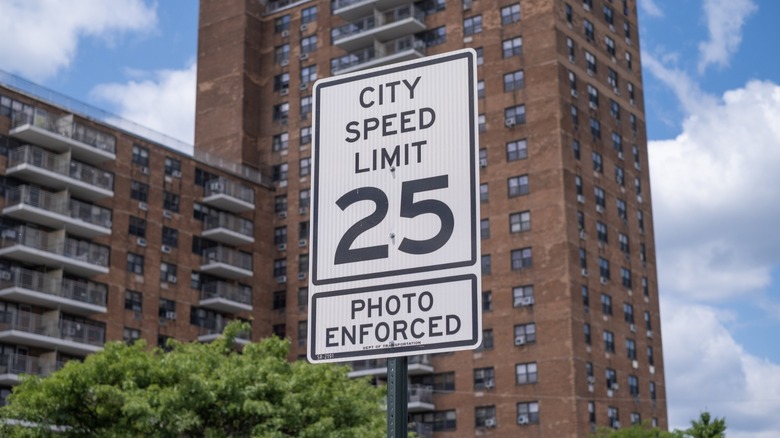 A city speed-limit sign reading "25 – Photo Enforced" stands in front of tall apartment buildings