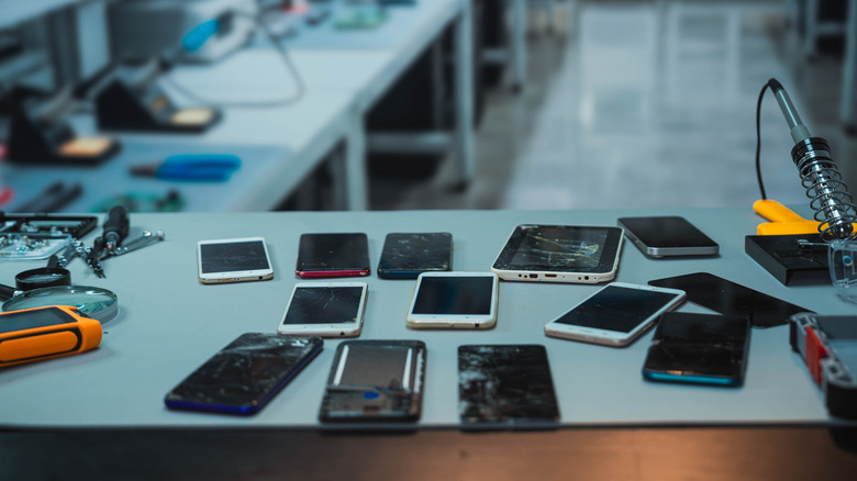 Several phones and electronics sitting on a workbench for repair