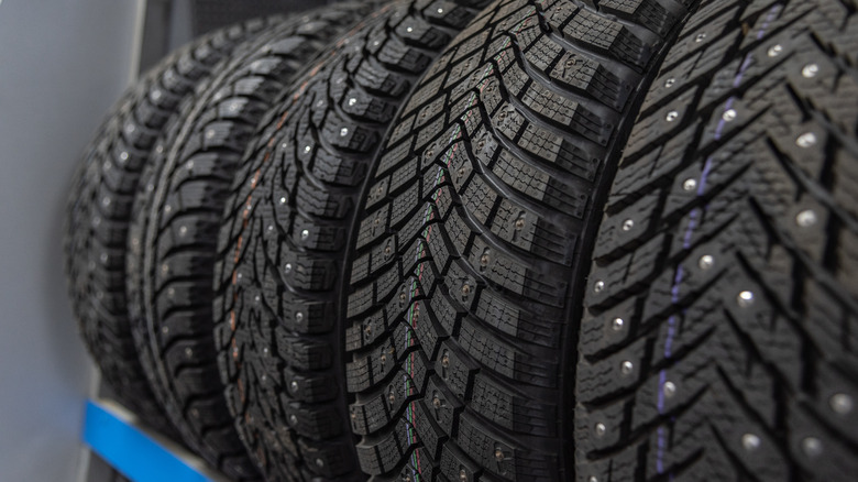 A row of black studded car rubber tires displayed on the shelf of a shop.