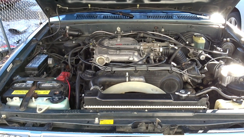 A Toyota 3VZ-E 3.0-liter, V6 engine sitting in the dusty engine bay of an unidentified, blue Toyota model from the 1990s.