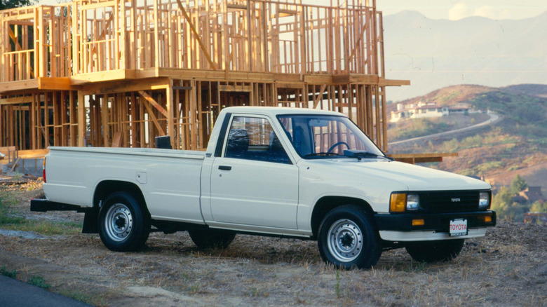A white "XtraCab" fifth-generation "Toyota Pickup" from 1985 standing in front of an under-construction house.