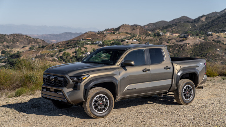 A browish 2026 Toyota Tacoma pickup truck standing on a muddy section of land offroad, with a valley in the back.