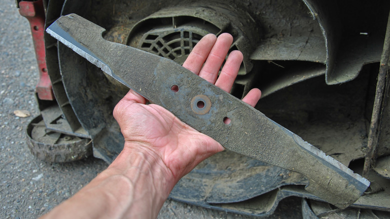 A dirty lan mower blade in held in the palm of a hand.