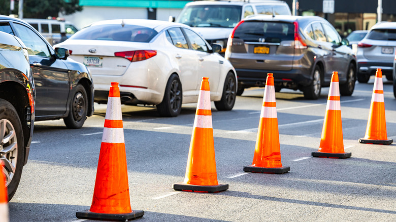 Traffic cones blocking lanes on a busy city street with cars and urban traffic during daytime in New York City.