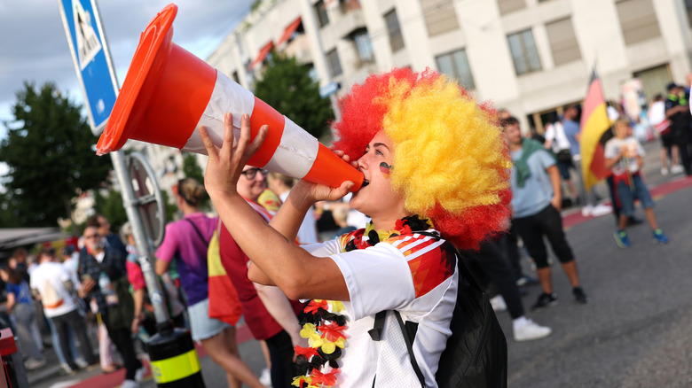 A soccer fan uses a traffic cone to yell support for her team before a match.