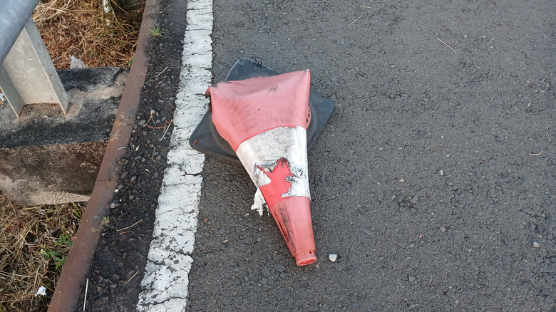 A flattened and broken orange traffic cone lying on an asphalt road after a vehicle ran over it.