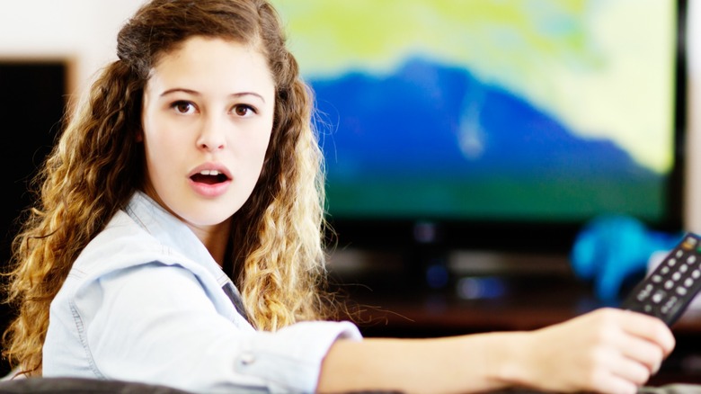 woman holding a TV remote control turns round from watching television