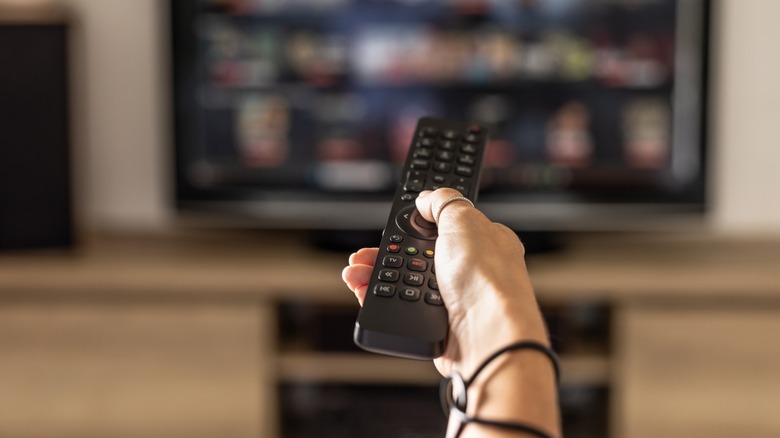 Close up of a person holding a control remote with a television screen on the background