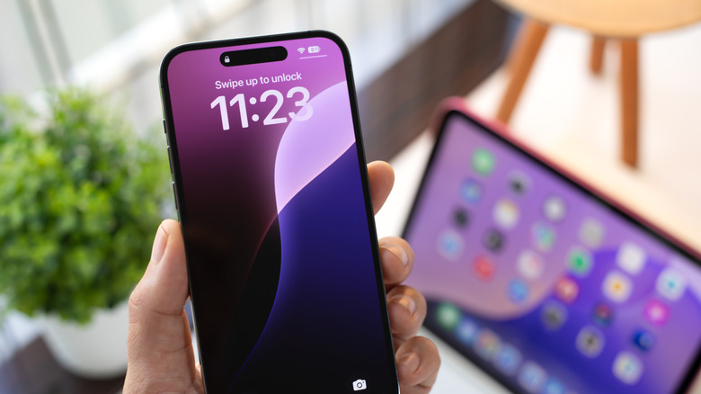 A person holding an iPhone with an iPad in the background