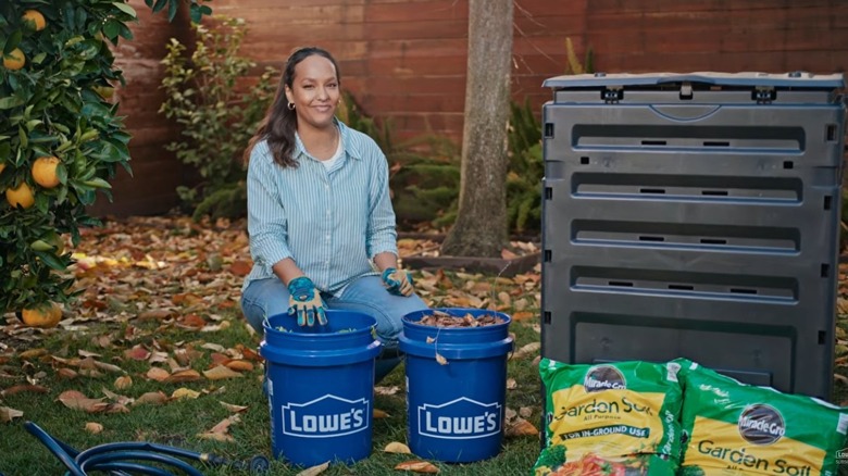A person in a garden poses with Lowe's buckets and potting soil.