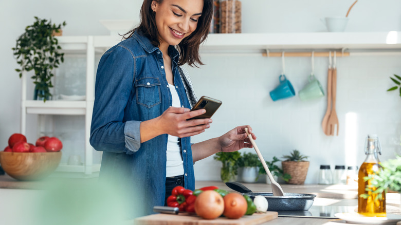 woman cooking in a kitchen while using her smartphone