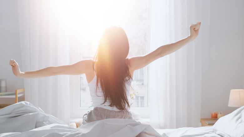 Woman stretching in bed with sunlight