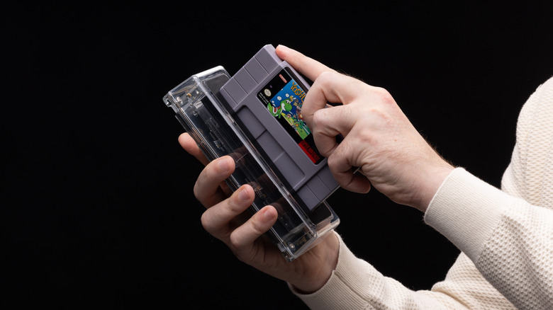 A person inserting a Super Nintendo cartridge into the transparent Epilogue SN Operator dock