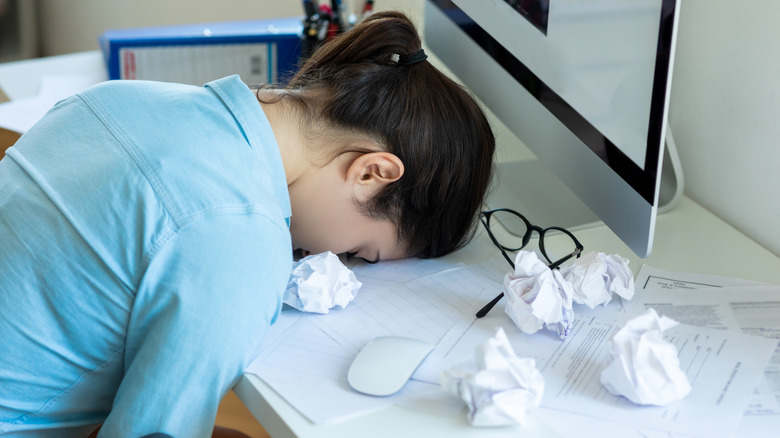 Woman with her face on her desk surrounded by crumpled paper