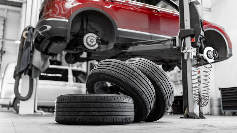 Wheels and tires stacked, with a red car on a lift in the background.