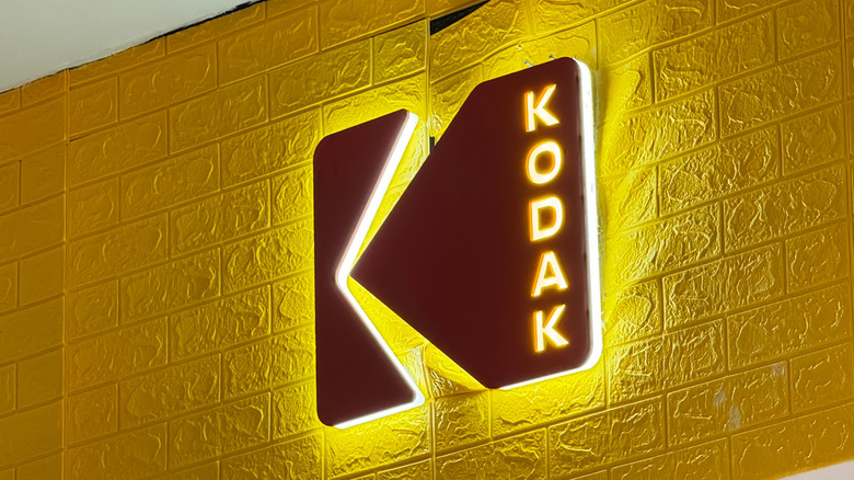 A lit Kodak sign on a yellow wall