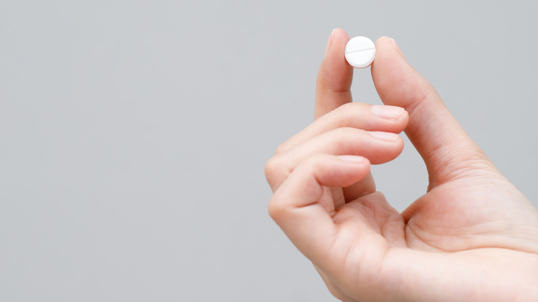 A person's hand holding a pill
