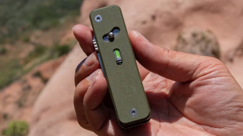Hand holding a green Roxon multitool outdoors
