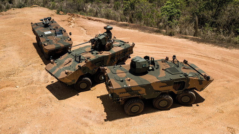 A trio of Iveco Guarani 6x6 amphibious vehicles in camouflage paint on a dirt road