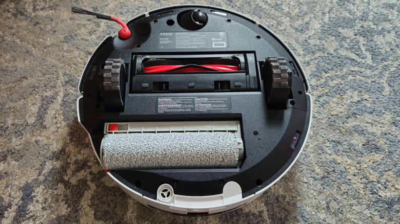 The Yeedi M14 Plus upside down showing the bottom wheels and roller on a blue carpet