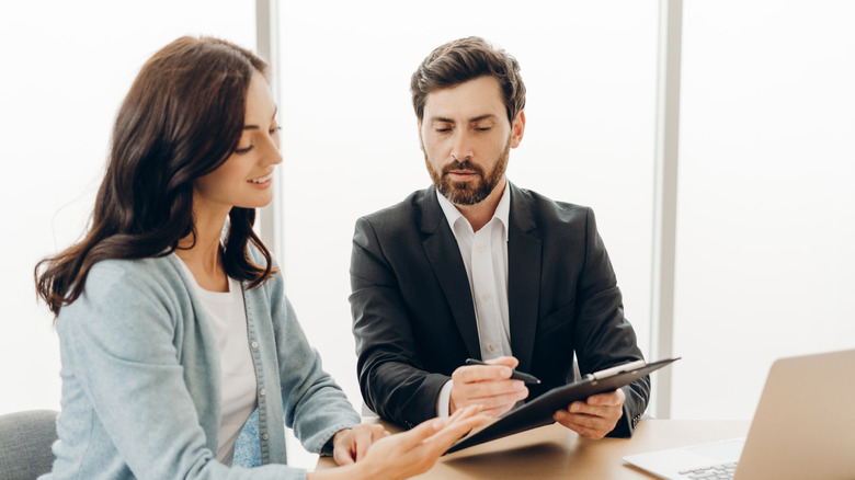 Two people in formal outfits looking at paperwork
