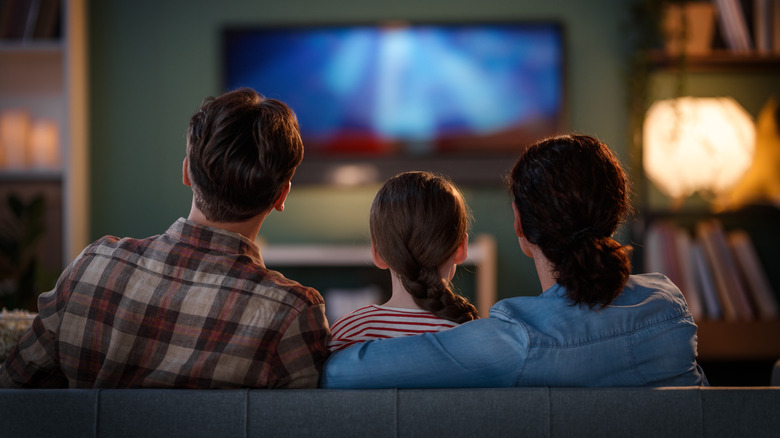 Man, child, and woman watching television on a sofa.