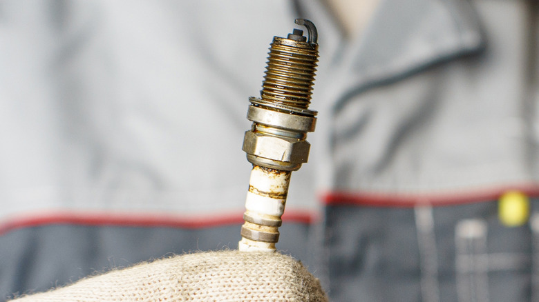 Close up of a gloved hand holding a used spark plug.